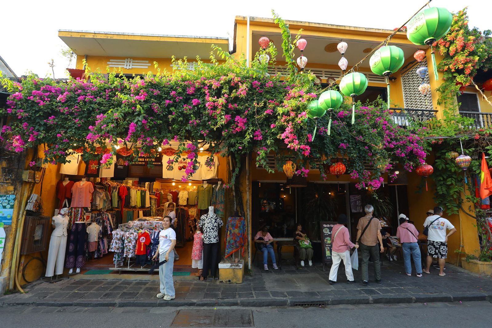 Shoppers outside a clothing shop hung with silk lanterns and bougainvillea in Hoi An, Vietnam